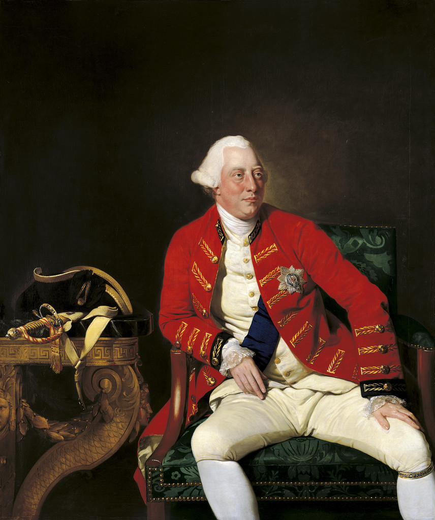 A three-quarter length portrait of George III, seated on a chair upholstered in green brocade, and leaning to the left: one elbow on the arm of the chair, the other hand propped on his thigh. He is wearing a powdered wig and scarlet military jacket with blue cuffs and gold braid embellishments over a white waistcoat, breeches and stockings. He also wears the blue sash and star of the Order of the Garter. On the table beside him are a tricorn hat and a sword with a decorative hilt.