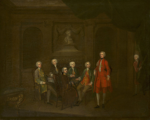 An oil painting of a group of men seated around a table in a dimly-lit room. A bust of Henry V is over the fireplace. All of them wear powdered wigs and fashionable frock coats. The most prominent figure stands to the right of the table in a striking red silk suit. Prince Frederick appears in the doorway on the far right, peering around a curtain.